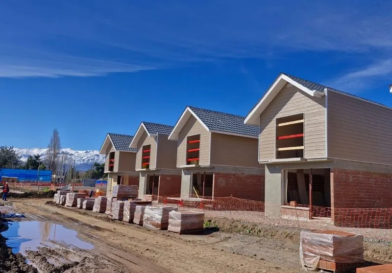 Fila de viviendas en construcción con primer nivel de ladrillo y revestimiento superior, con la cordillera nevada de fondo