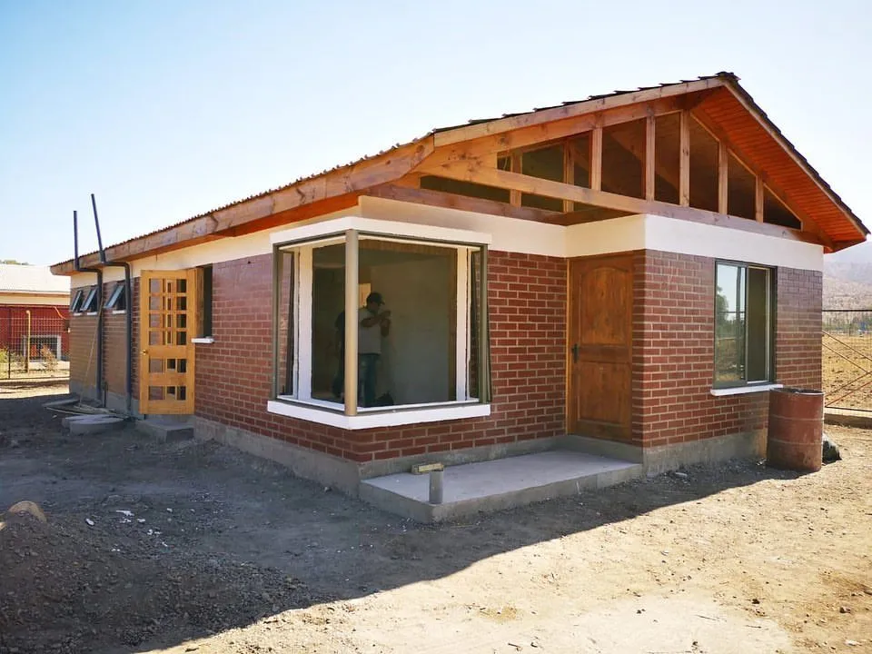 Casa de ladrillo de un piso en etapa final de obra, con la estructura de techumbre de madera a la vista, en un entorno rural