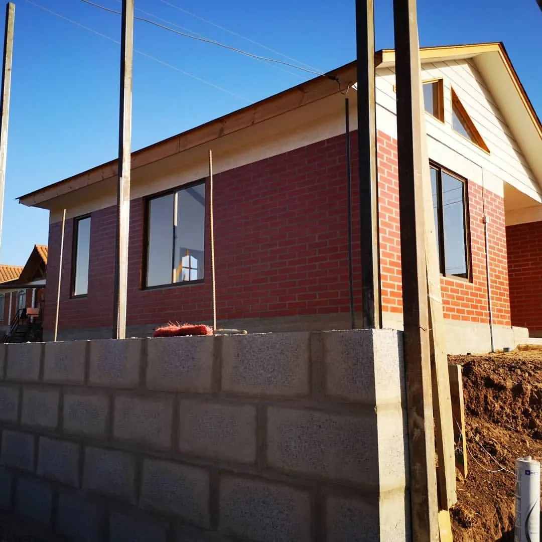 Casa de ladrillo en construcción, levantada sobre un muro de contención de bloques de hormigón