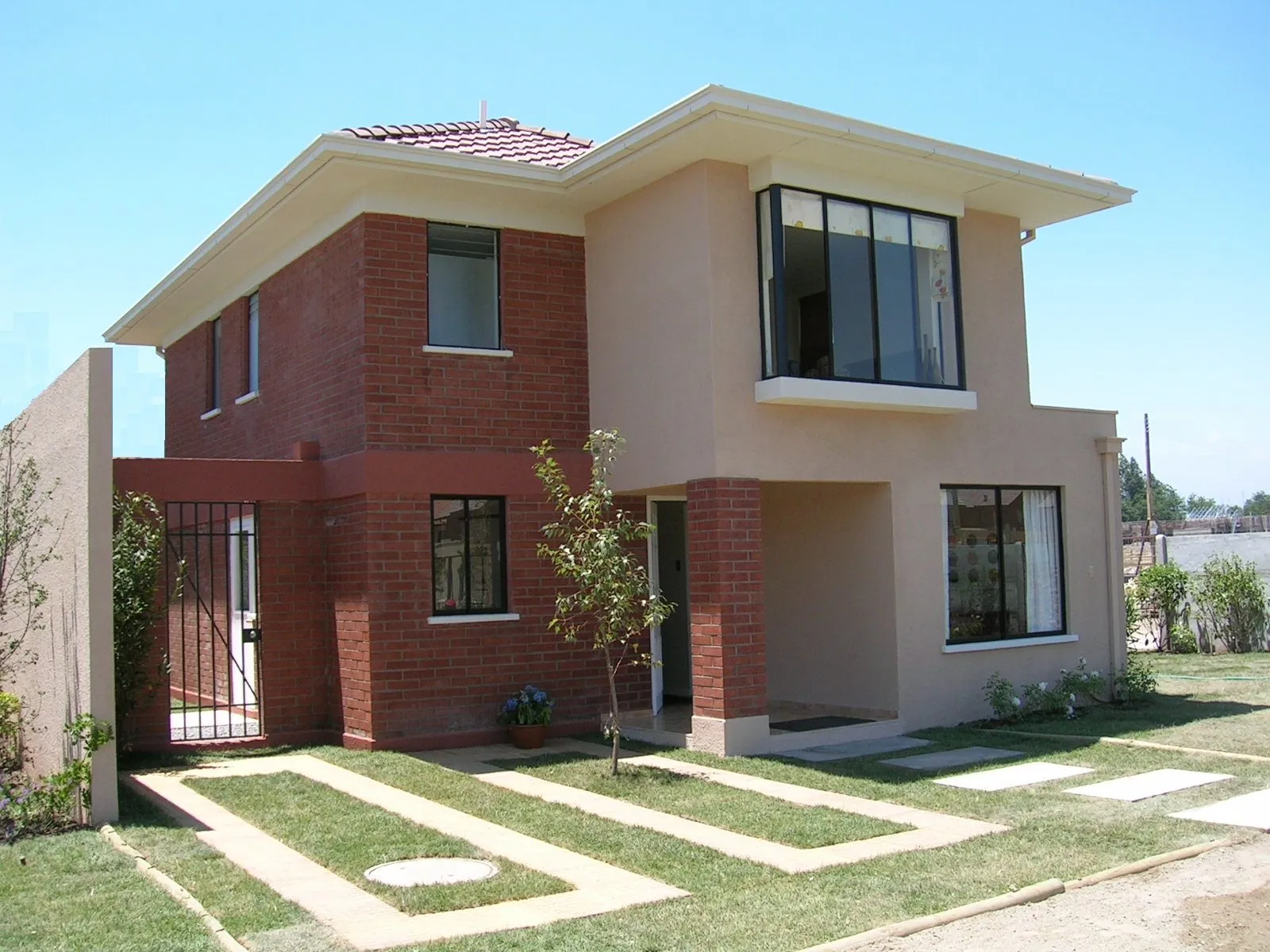 Casa familiar de dos pisos con fachada de ladrillo a la vista, jardín y reja de acceso